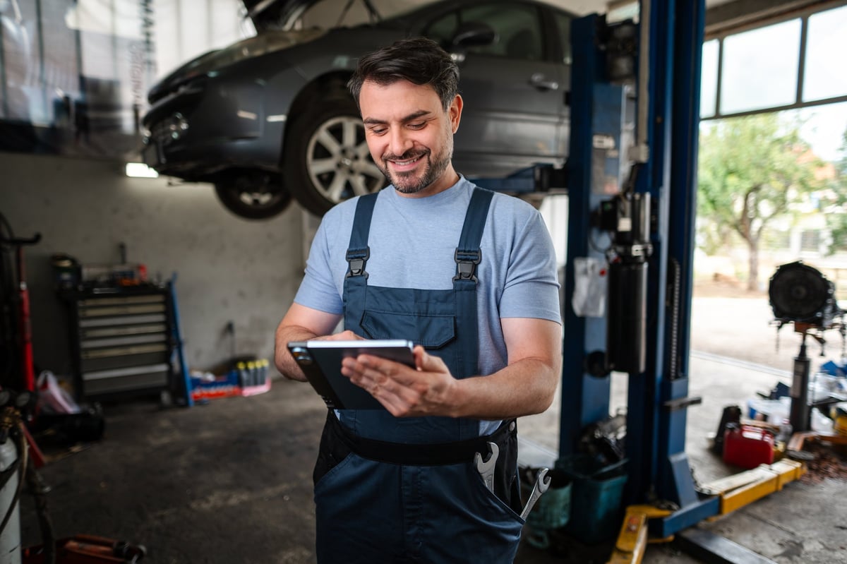 Mechanic using a tablet beside a car raised on a hoist in the workshop